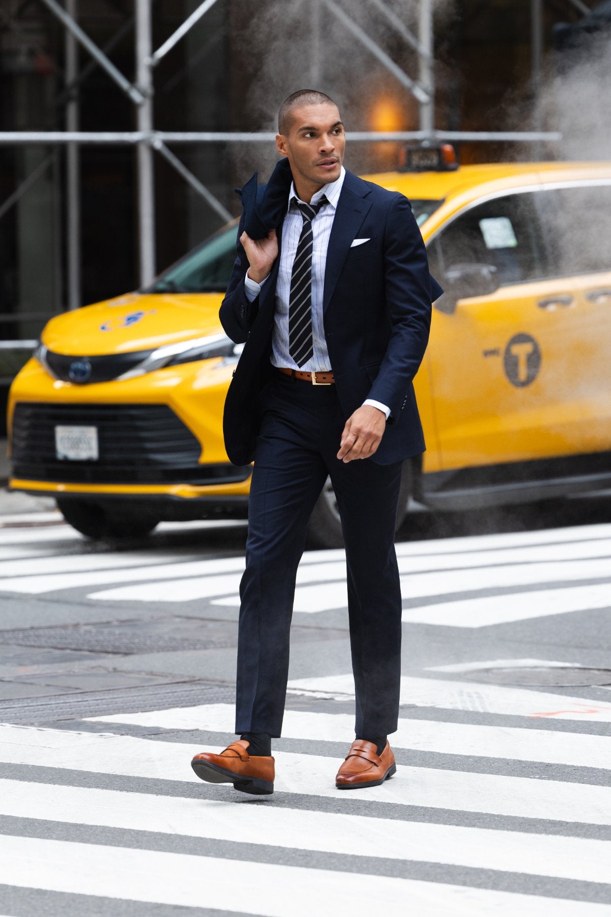 Man in a navy suit crossing the street past a taxi in whiskey Capital Loafers