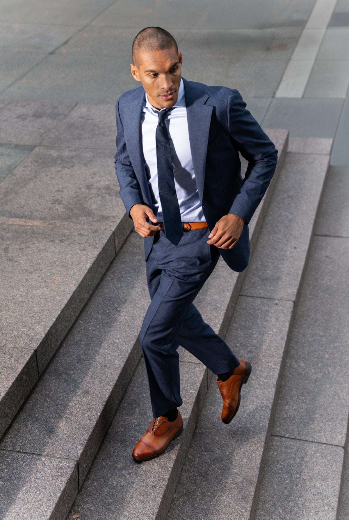 Man in a navy suit bounding up granite steps in whiskey Capital Oxfords
