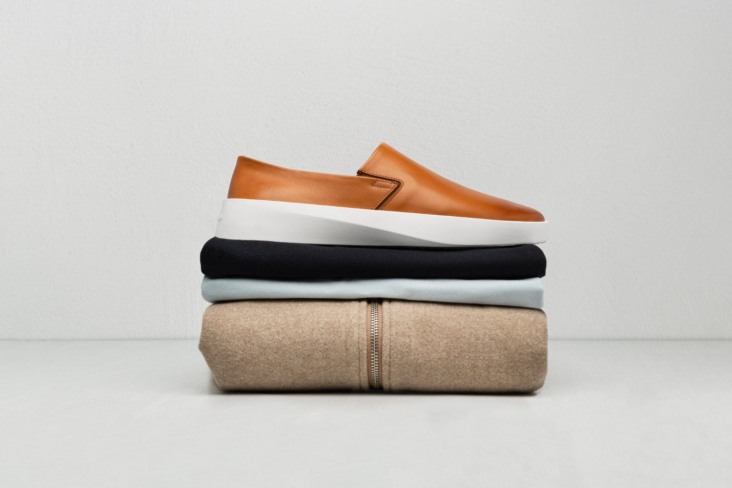 Honey leather slip-on above a stacked set of clothes. 