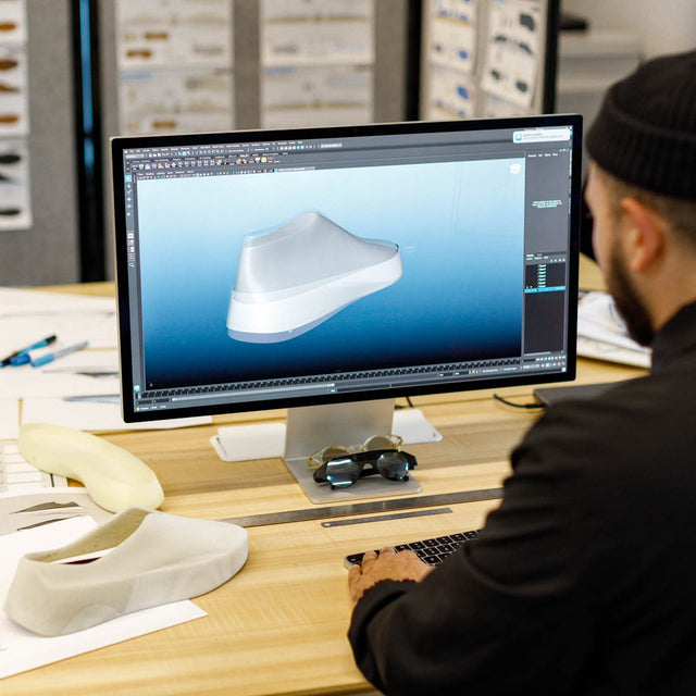 Designer wearing beanie working on a computer displaying a shoe design