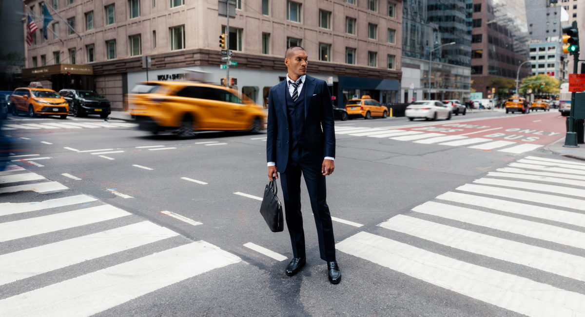 Man in a navy three-piece suit standing in a Manhattan crosswalk in black Capital Loafers