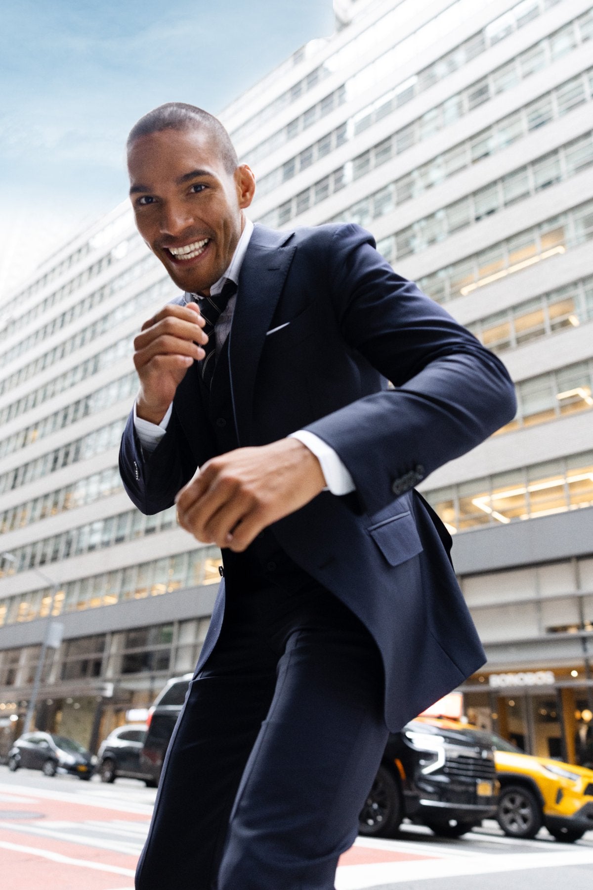 Man in a navy three-piece suit grinning on a Manhattan street